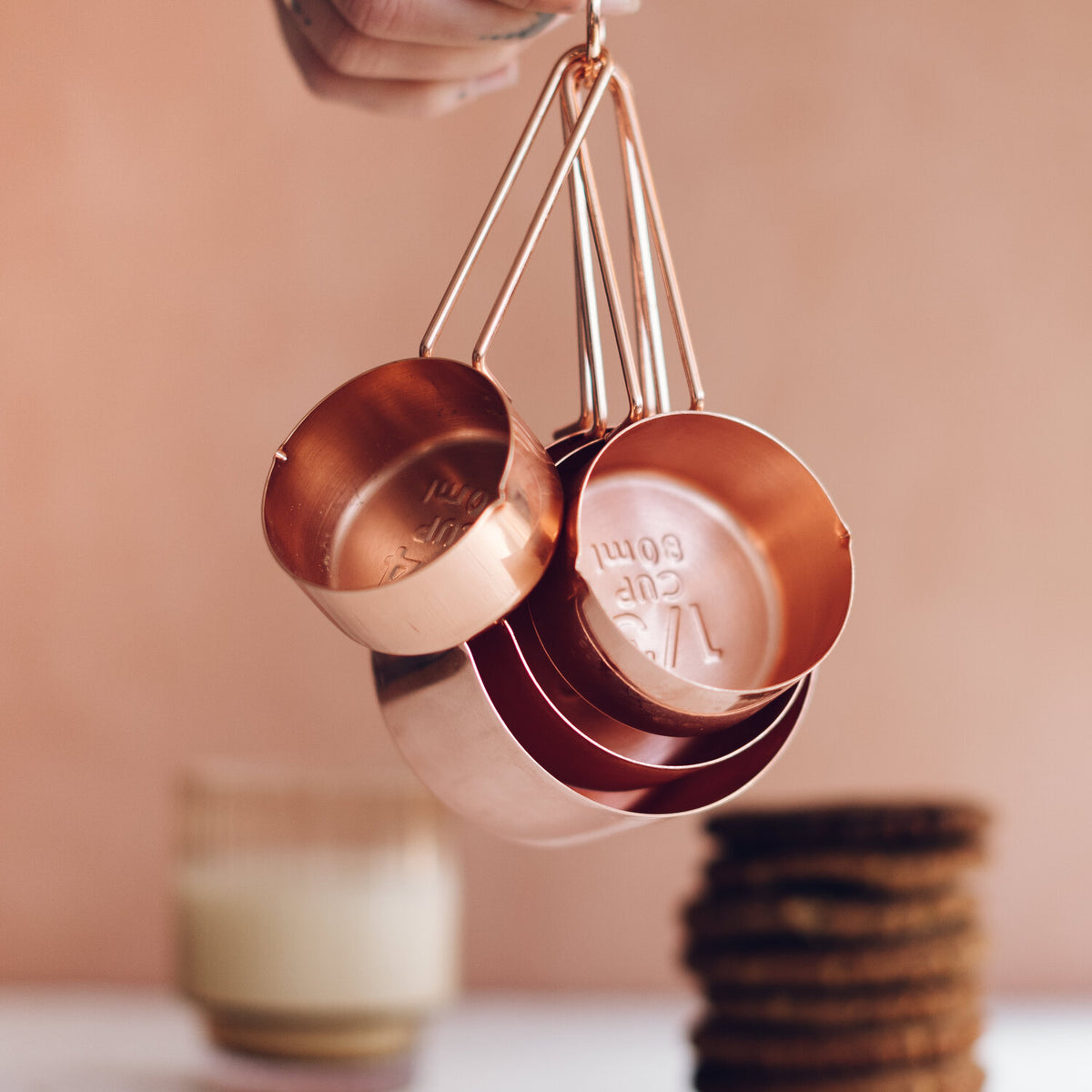 Copper Measuring Cups hanging on their ring in front of a candle and a stack of biscuits