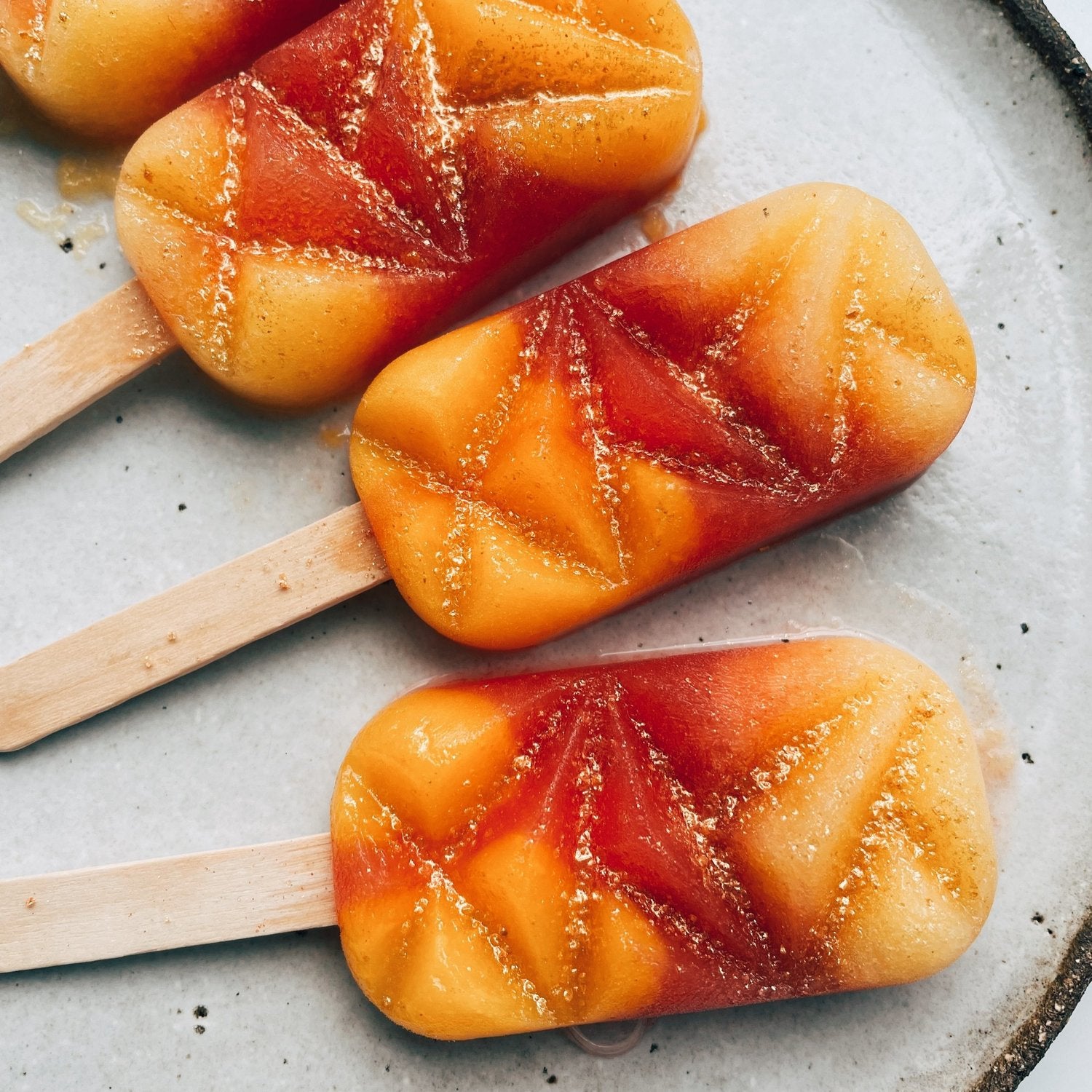 Layered mango and berry ice blocks in the faceted crystal shape, on wooden sticks