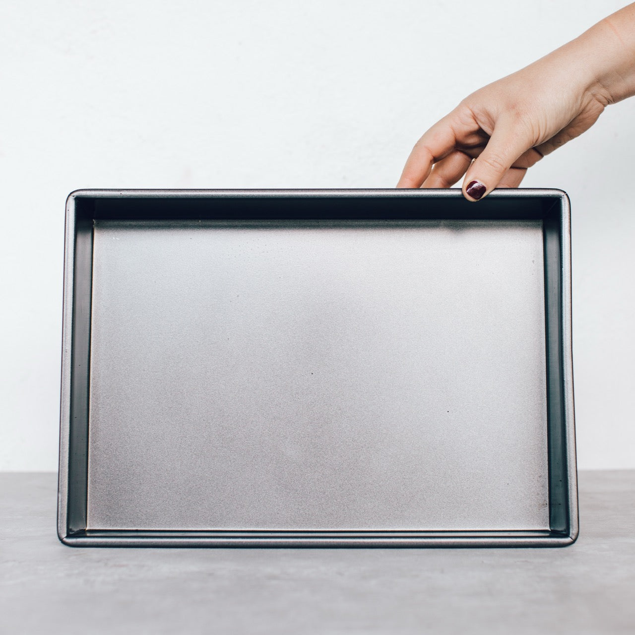 Deep Sheet Pan in dark non-stick steel, held at one edge