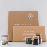 Thermo Deluxe Slide and Deluxe Tray in their kraft gift boxes on a bench with storage jars