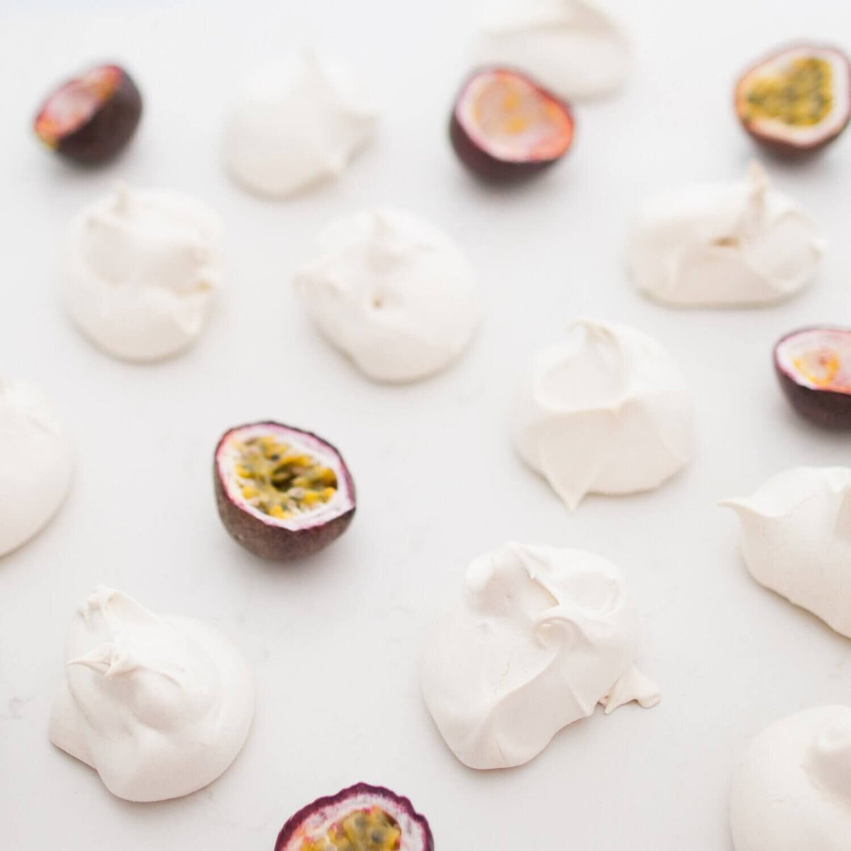 Meringue nests scattered with halved passionfruit on a white surface, from the Desserts Class Booklet