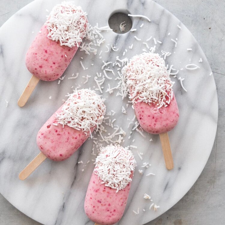 Strawberry ice creams dipped in white chocolate and coconut, arranged on a marble board