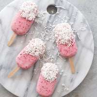 Strawberry ice creams dipped in white chocolate and coconut, arranged on a marble board
