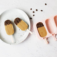 Two chocolate-dipped caramel ice creams on a plate with cocoa nibs scattered around