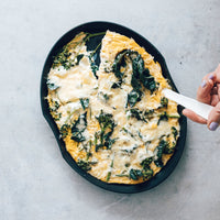 Baked spinach and cheese frittata in a dark pan being lifted with a spatula