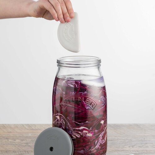 Hand lowering the ceramic weight into the Fermentation Set jar of red cabbage