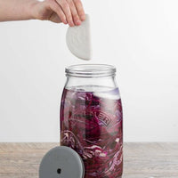 Hand lowering the ceramic weight into the Fermentation Set jar of red cabbage