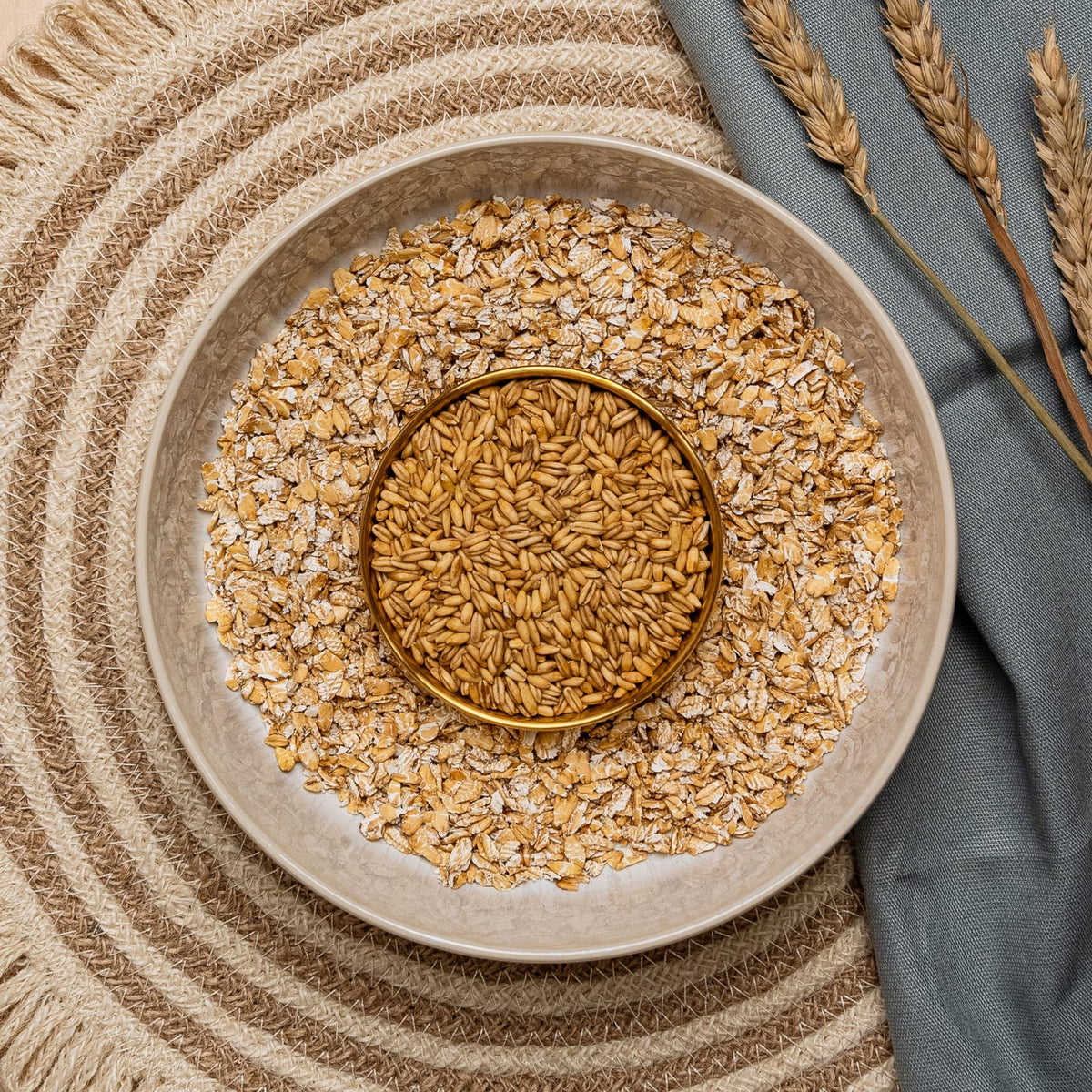 Bowl of freshly rolled oats surrounded by whole grains and dried wheat stalks