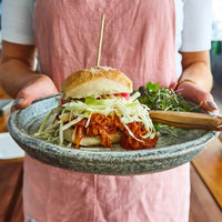 Hands holding a bowl with a loaded vegan burger and slaw, from Hearty Vegan Thermo Cooked