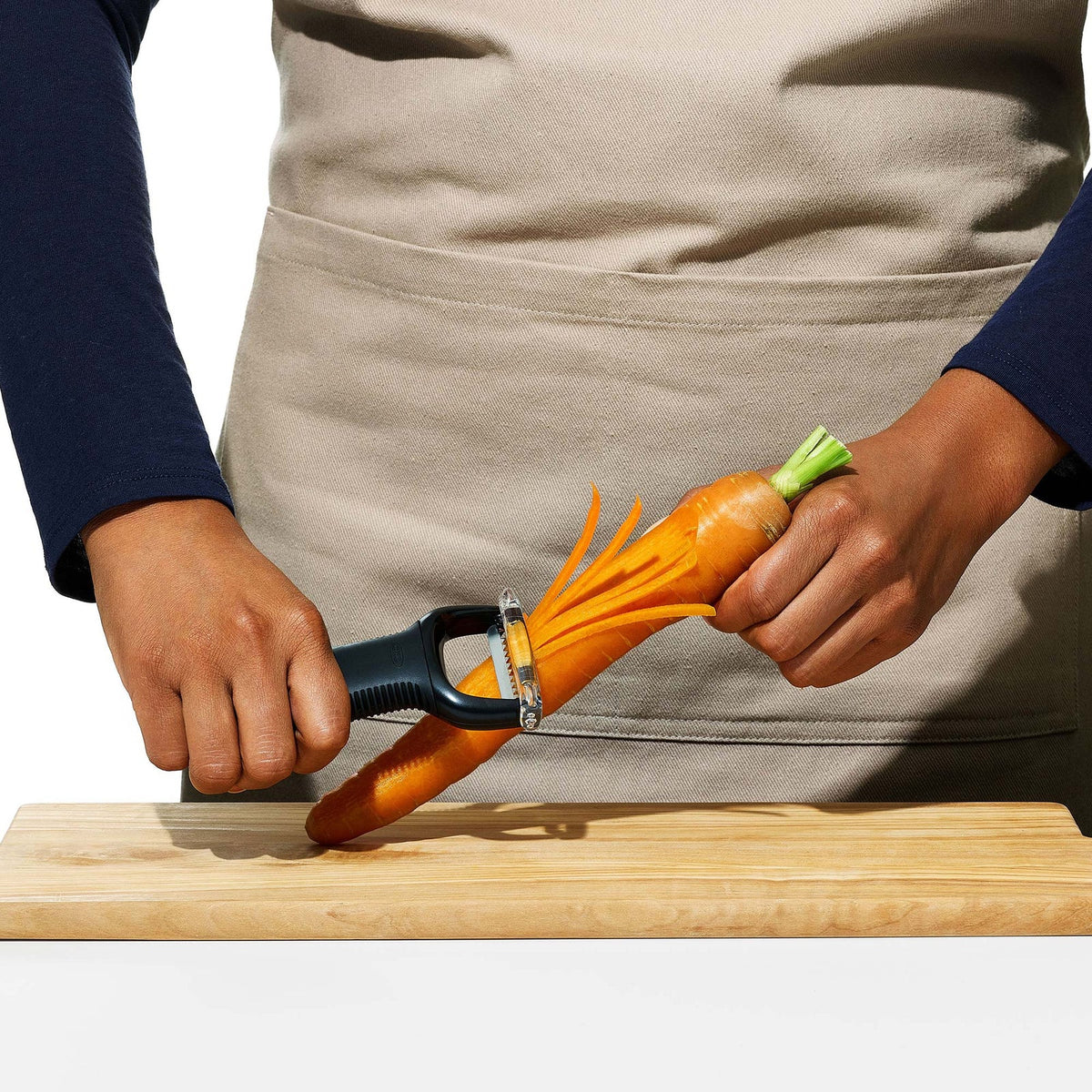Julienne Peeler being drawn down a carrot on a wooden board, producing long even matchsticks