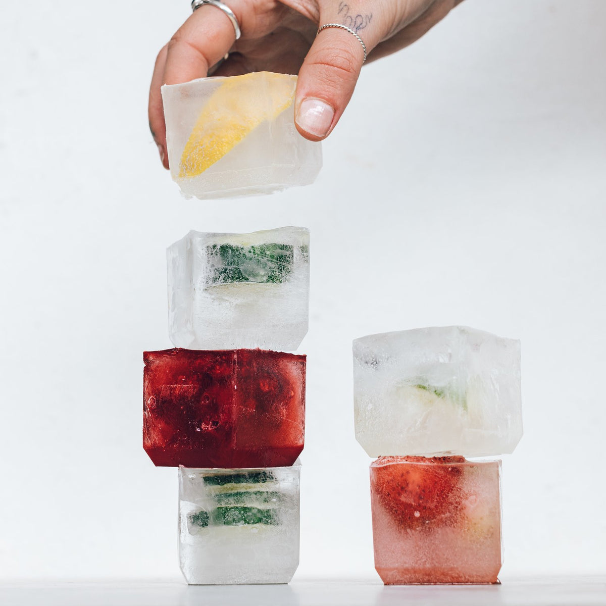 Hand lifting a jumbo ice cube from a stack of cubes with herbs and berries frozen inside