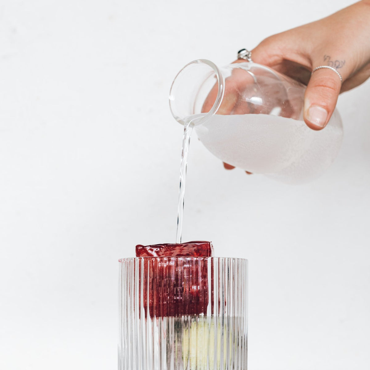 Jug pouring liquid over a jumbo ice cube in a ribbed glass
