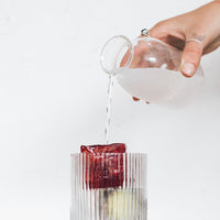 Jug pouring liquid over a jumbo ice cube in a ribbed glass