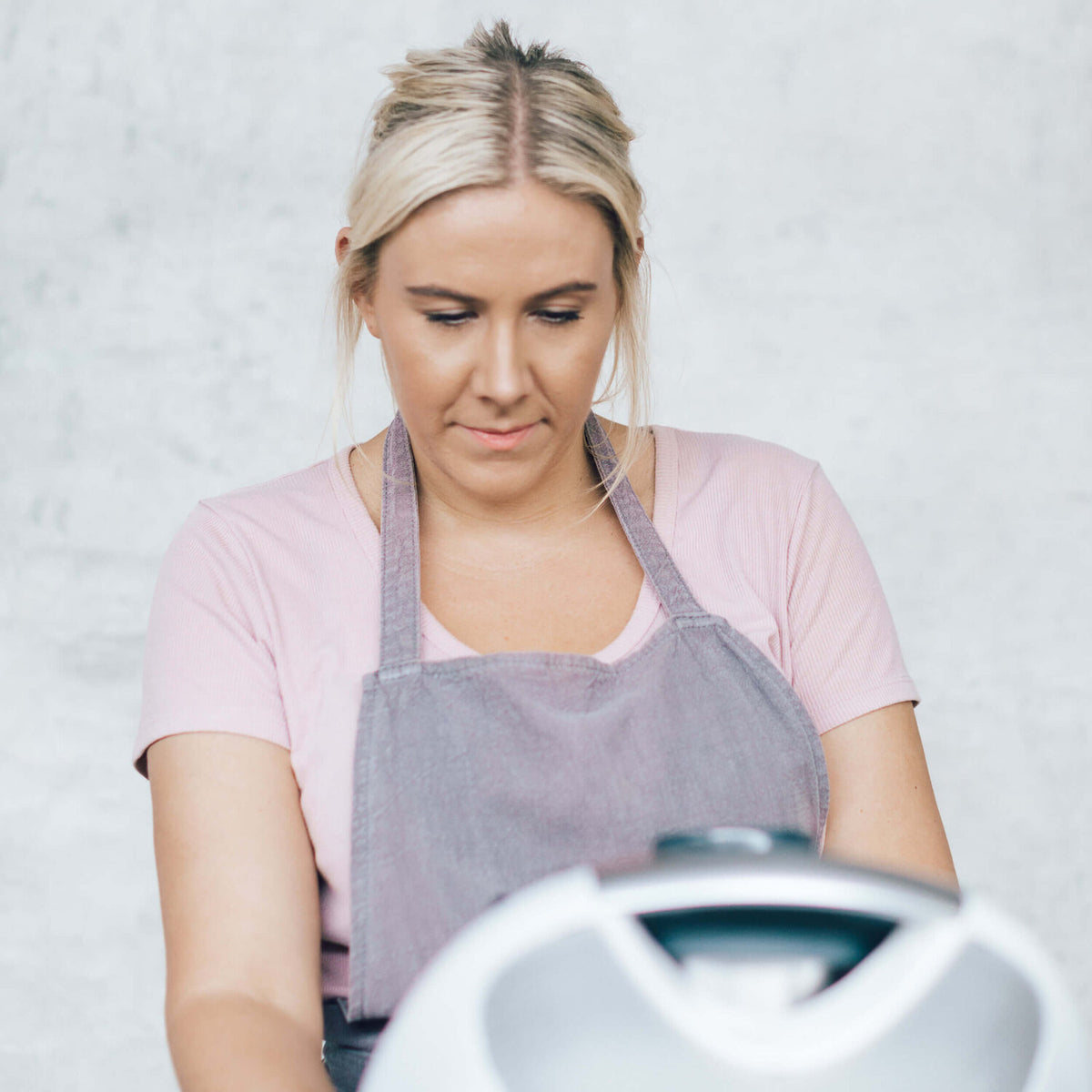 Woman in a blush pink Linen Apron working at a bench beside a Thermomix