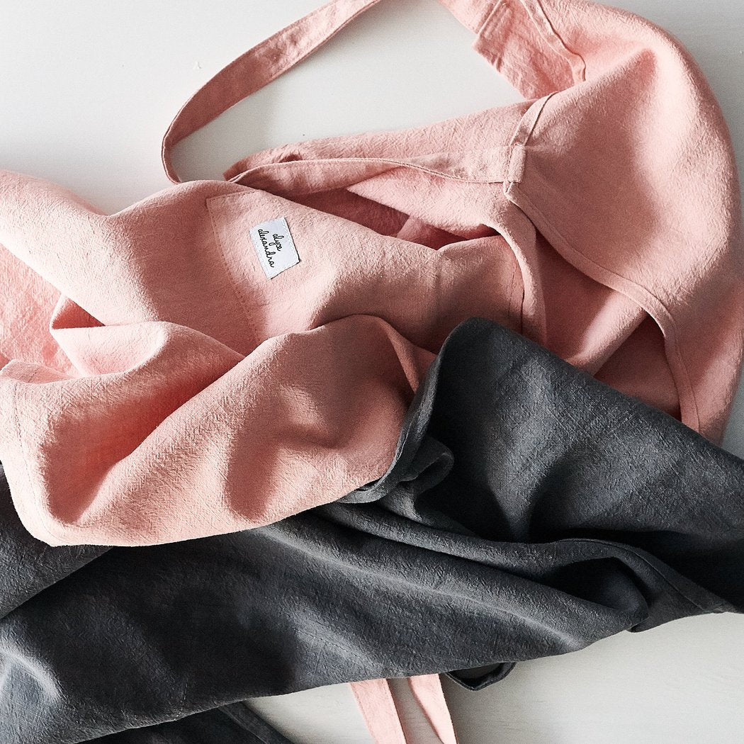 Blush pink and charcoal Linen Aprons folded together to show the linen texture