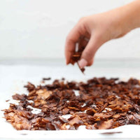 Hand picking up a piece of crispy coconut bacon from a plate