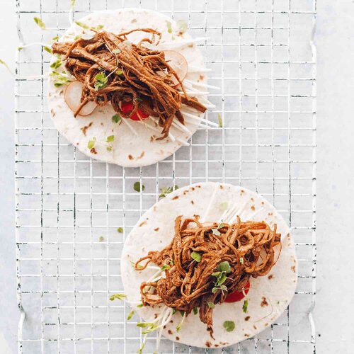 Two soft tacos filled with smoky pulled jackfruit and slaw on a wire rack