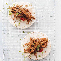 Two soft tacos filled with smoky pulled jackfruit and slaw on a wire rack