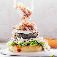 Loaded burger with smoky filling, salad and sauce on a wooden board