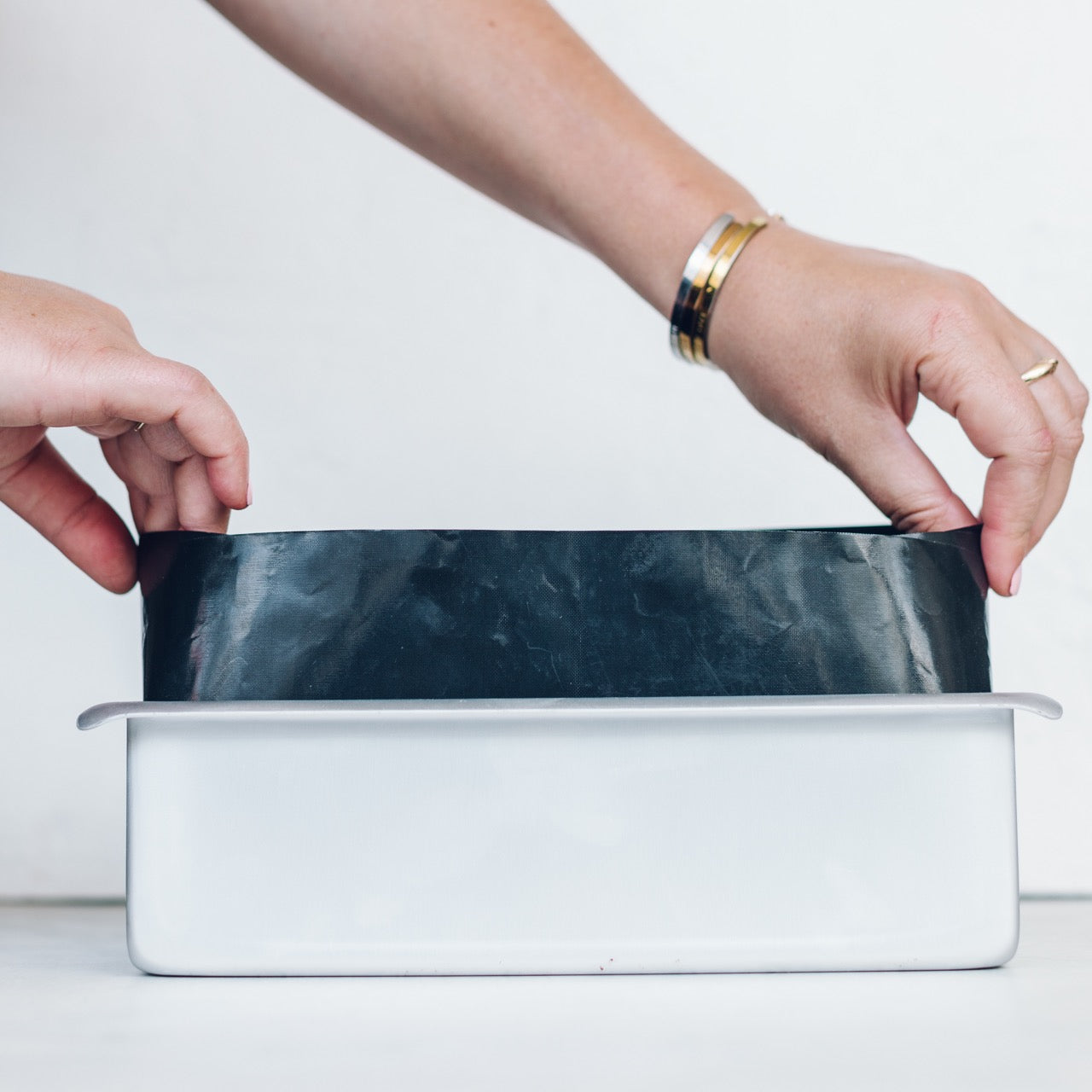 Hands pressing dough into the Loaf Tin on a bench