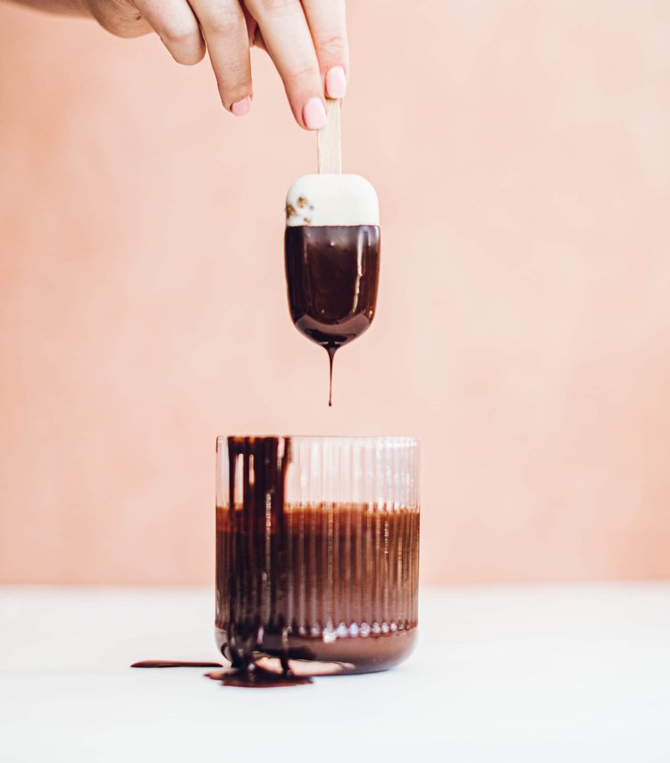 Hand dipping a mini ice cream into a glass of melted dark chocolate