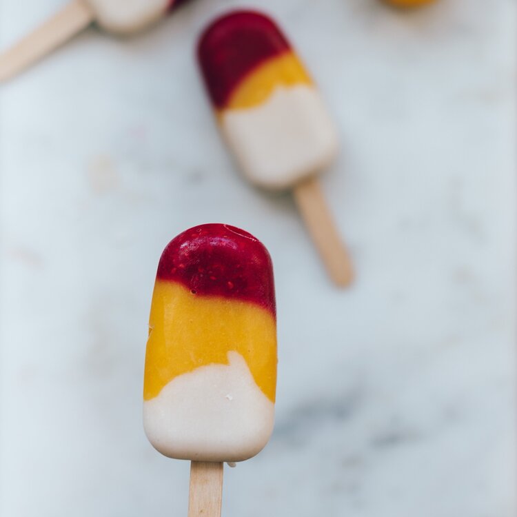 Two mini layered ice blocks in mango and berry, standing on a marble surface