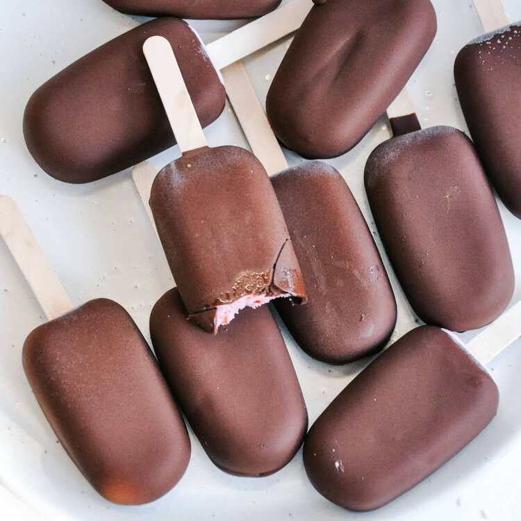 Pile of chocolate-coated mini ice creams, one bitten to show the pink centre