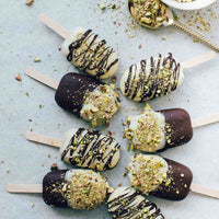 Mini ice creams dipped in dark chocolate and drizzled with pistachio, laid out on a pale surface