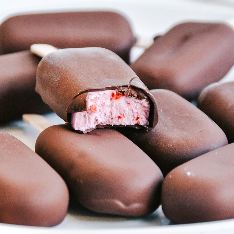 Chocolate-coated mini ice creams piled together, one bitten to show the strawberry centre