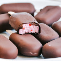 Chocolate-coated mini ice creams piled together, one bitten to show the strawberry centre