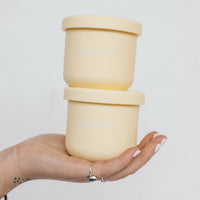 Hand holding a stack of yellow Mini Silicone Pot Containers with their lids on