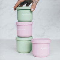 Hand stacking sage green, pink and yellow Mini Silicone Pot Containers together