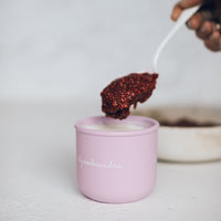 Hand spooning berry compote into a pink Mini Silicone Pot Container on a pale bench