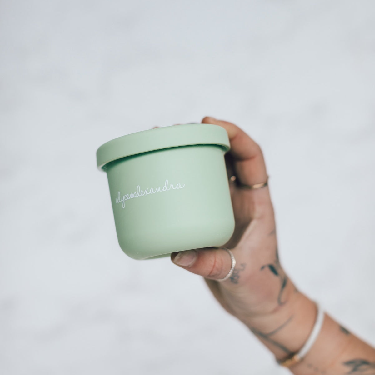 Hand holding a sage green Mini Silicone Pot Container with the lid on