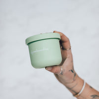 Hand holding a sage green Mini Silicone Pot Container with the lid on