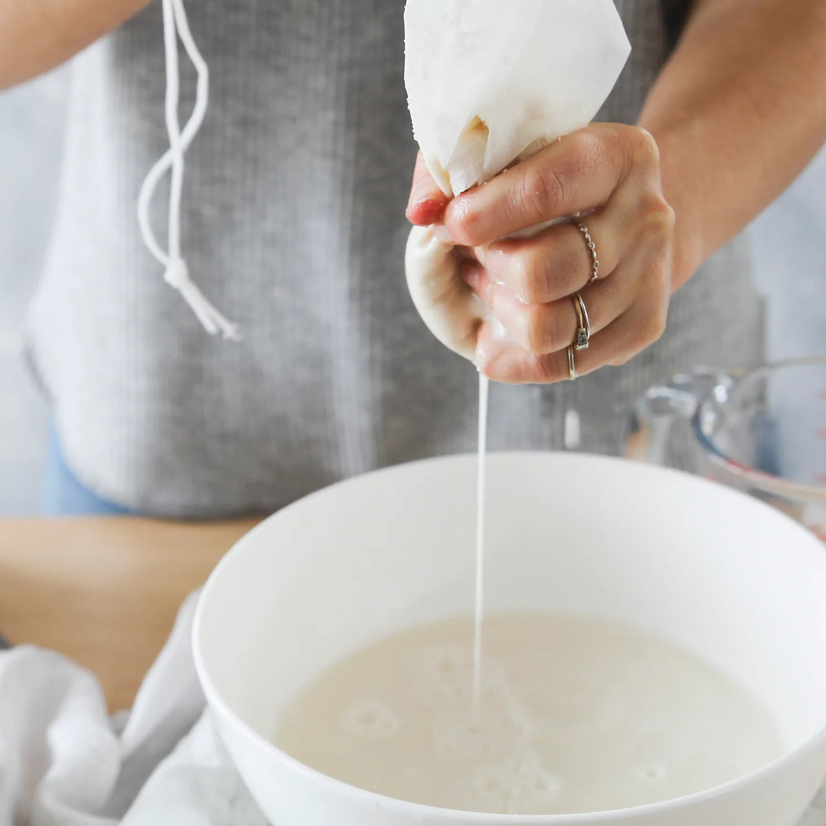 Hands squeezing the Nut Milk Bag to strain the last of the nut milk into a bowl