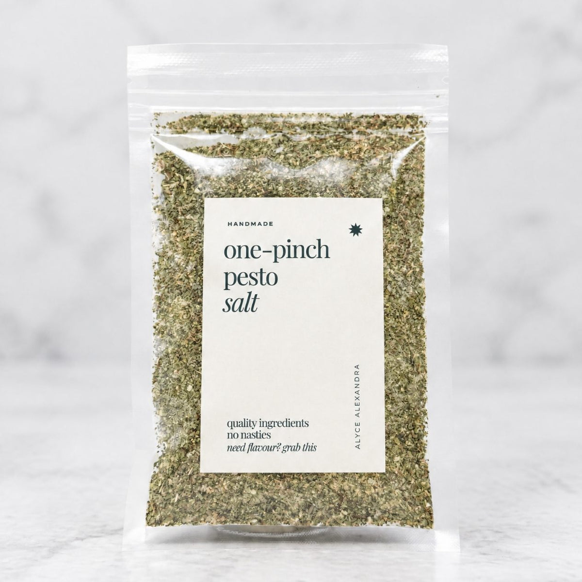 Alyce's One-Pinch Pesto Salt in a clear 100g packet with a cream label and deep green lettering, the green basil-flecked salt visible through the front