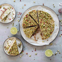 Lime and pistachio cake cut into wedges on a plate with fresh limes, from the Paleo Class Booklet