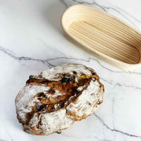 Oval rattan proving basket behind a scored fruit sourdough loaf of bread