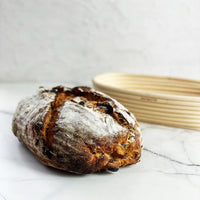 Fruit sourdough loaf of bread resting against the oval rattan proving basket