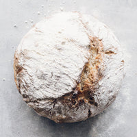 Round sourdough loaf of bread dusted with flour, proved in the round rattan basket