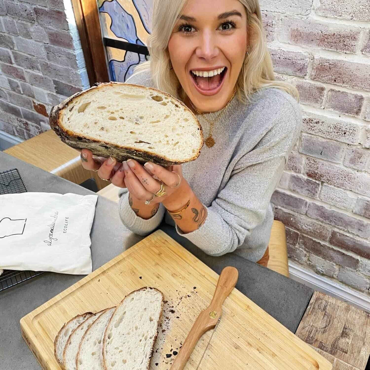 Woman holding up a sliced sourdough loaf of bread beside a board and bread knife