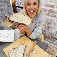 Woman holding up a sliced sourdough loaf of bread beside a board and bread knife