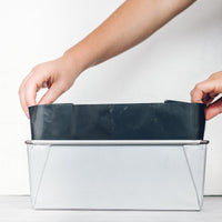 Hands lowering the Reusable Rectangular Loaf Tin Liner into a metal loaf tin