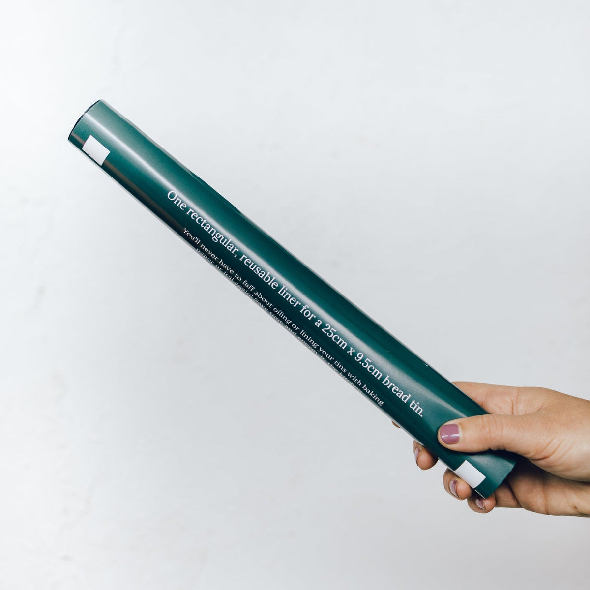Hand holding the Reusable Rectangular Loaf Tin Liner in its slim green packaging tube