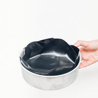 Hand holding the Reusable Round Cake Tin Liner fitted inside an empty cake tin