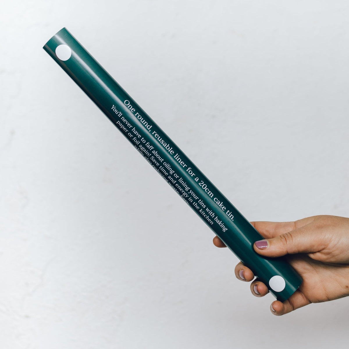 Hand holding the Reusable Round Cake Tin Liner in its slim green packaging tube