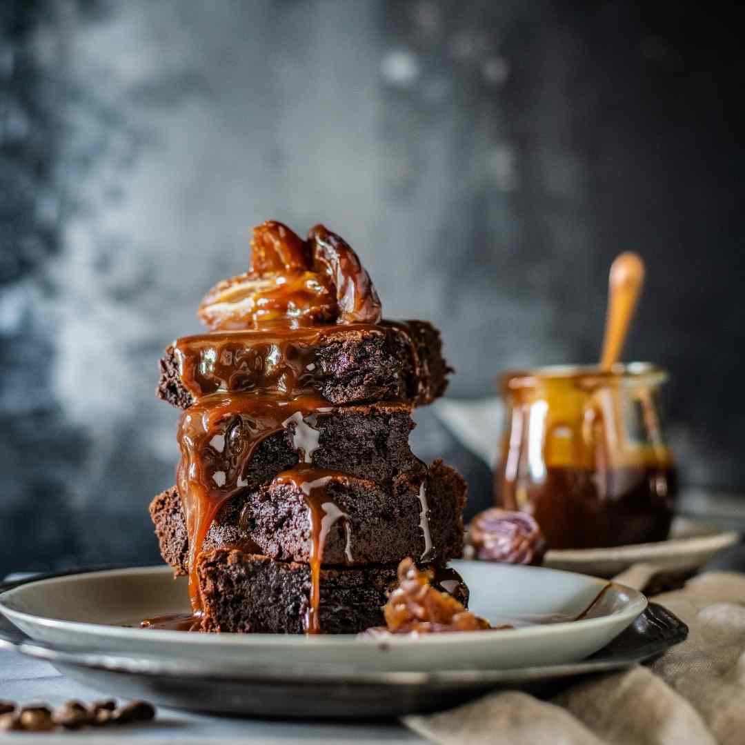 Stack of caramel brownies with sauce poured over, baked using the Reusable Sheet Cake Liner