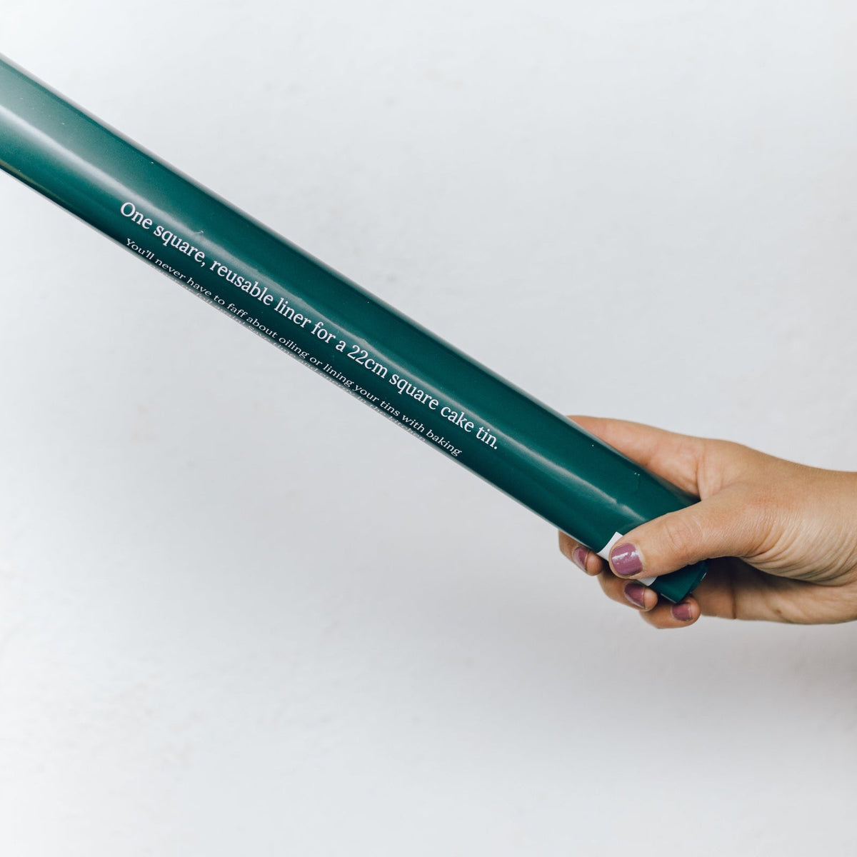 Hand holding the Reusable Square Cake Tin Liner in its slim green packaging tube