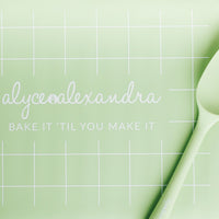Close-up of the sage green Silicone Baking Mat showing its grid markings and bake it 'til you make it print